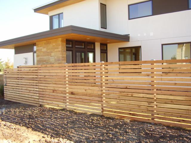 Horizontal slatted wood fence panels enclosing a contemporary two story house