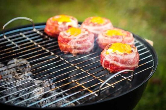 Two zone cooking charcoal grill with bacon wrapped beef patties and and egg on top