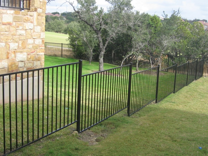 Iron fence enclosing a big backyard with a gradual slope in Central Texas