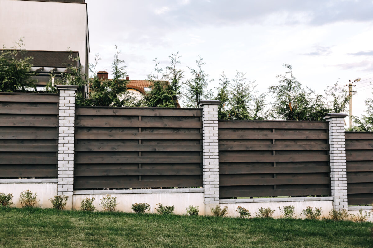 Horizontal tiered sections of brown wooden boards fence and white brick pillars on a slope