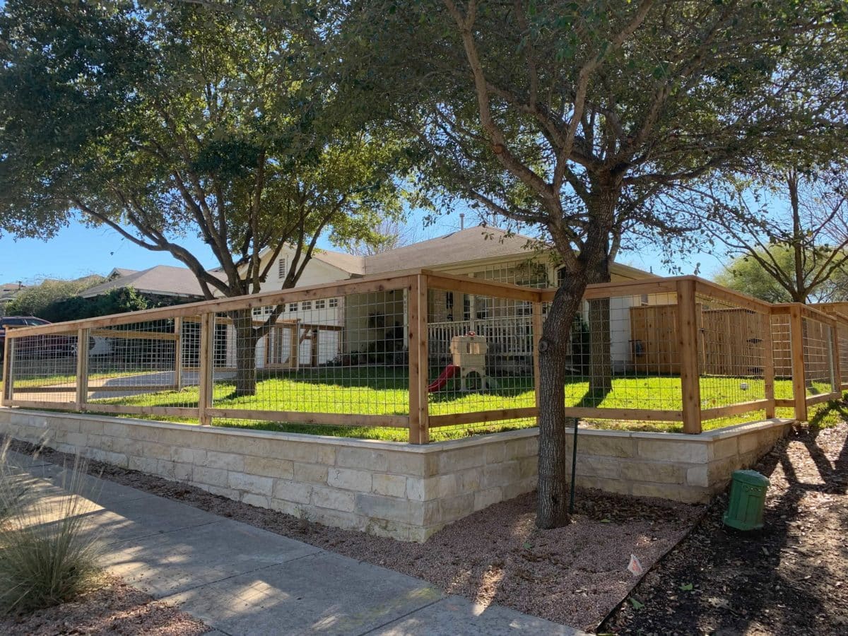 Wooden framed bull wire fence over a retaining beige brick wall enclosing the front yard of a house in Austin