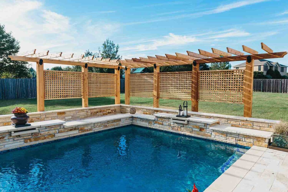 L-shaped wood pergola enclosing a part of a pool with a lattice screen for added privacy