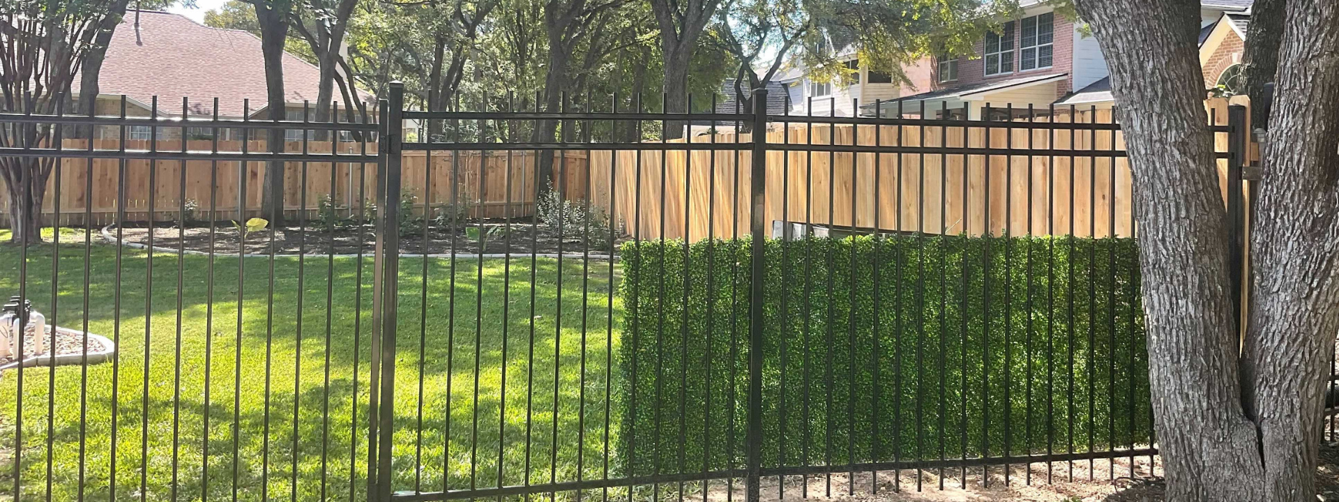 Wood fence and iron fencing of a big backyard in an Austin property, two parts of the backyard are enclosed by wood fence and the other parts by iron fence