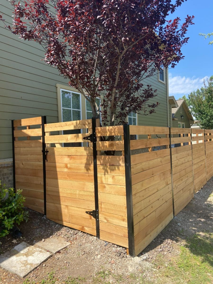 Horizontal wood fence with top slats on the corner of a backyard with a beautiful purple-leafed tree