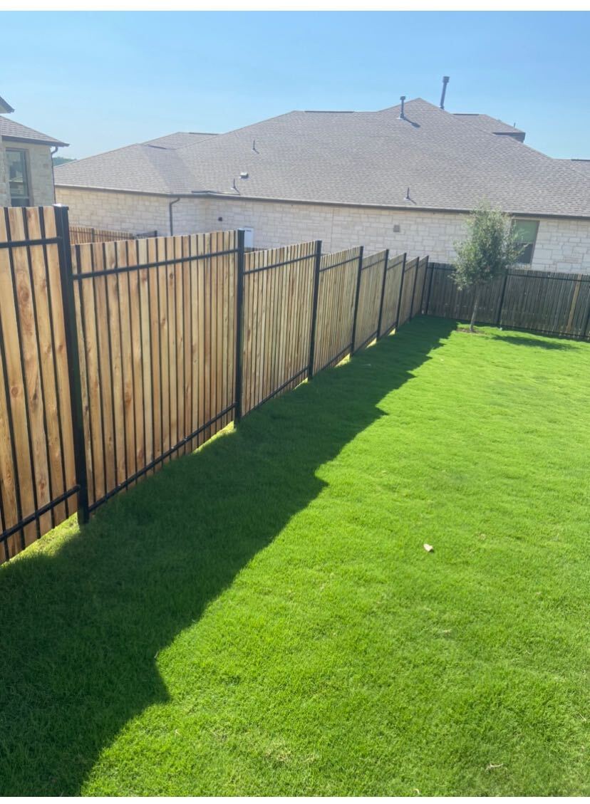 Picket iron fence with cedar slats on a sloped backyard of an Austin house with very bright green grass