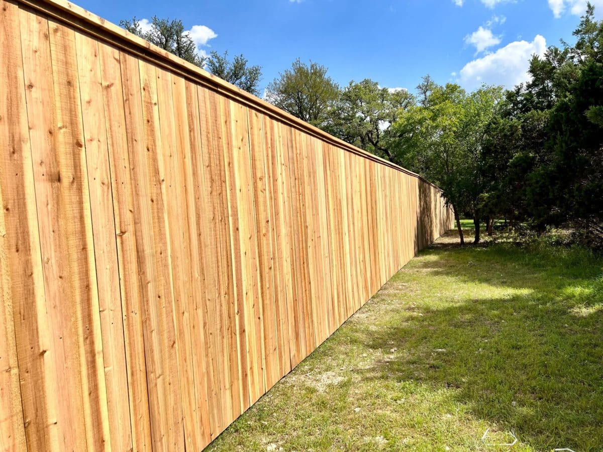 Long wood fence with cap board on grass next to trees and blue skies