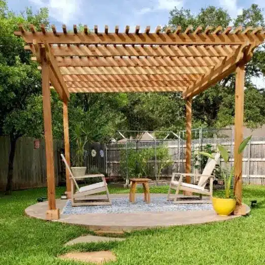 Wood pergola over two wood chairs and a table a rounded cemented area in the center of a backyard in Austin, Texas