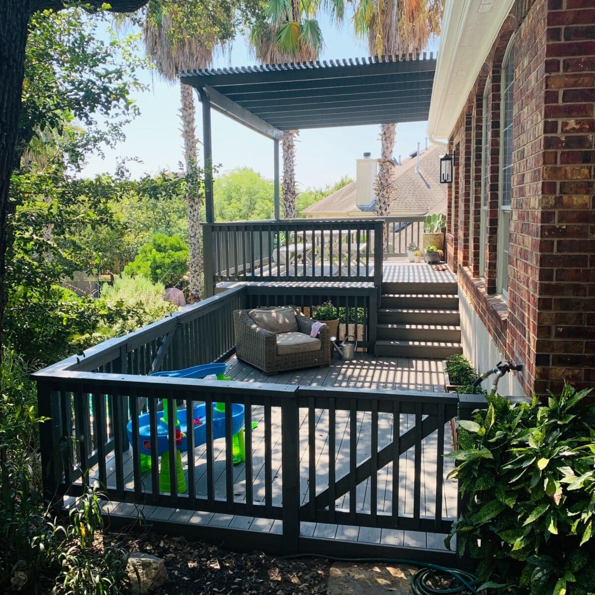 Side view of a two story pergola over wood deck with wood railings and wood gate to the background to keep children safe