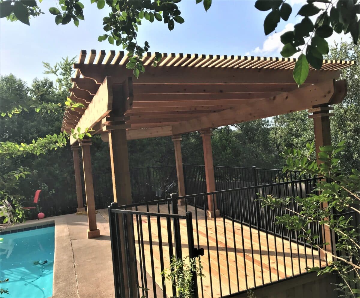Patio cover over a wooden deck next to a pool with iron railings and gate to keep children safe from the pool